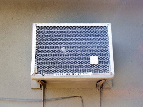Old and outdated window air conditioning unit manufactured by Emerson Quiet Kool mounted on the side of a home, showing signs of wear and inefficiency.